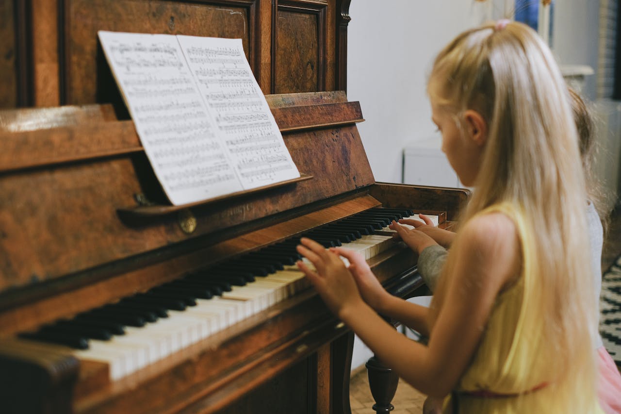 Prestations Two young girls playing piano together indoors, focused on a music sheet.